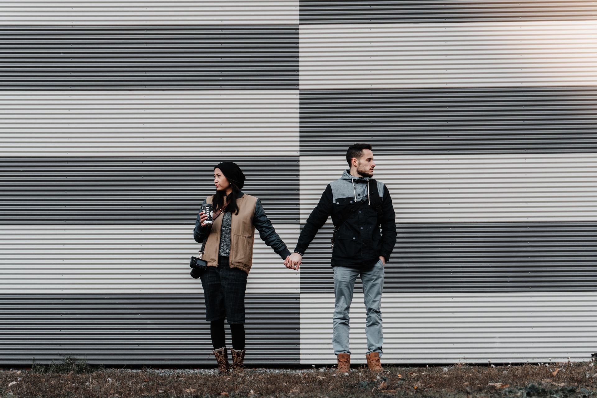 Paar, Hand in Hand vor einer gestreiften Wand, die Blick in unterschiedliche Richtungen